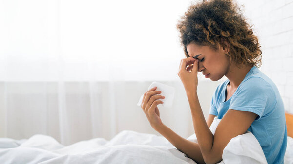 Молодая больная женщина с гриппом сморкается, сидит в постели, боковой вид, копирует пространство
