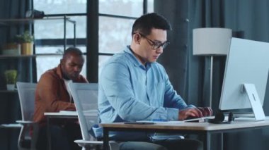 Masada oturan ve bilgisayar kullanmaya odaklanmış bir adam. Klavyede daktilo ediyor, dikkatlice ekrana bakıyor..