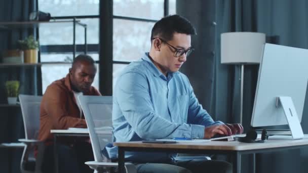 机の上に座っている男は コンピュータを使うことに集中した 彼はキーボードに入力し スクリーンを意図的に見ています ロイヤリティフリーストック映像