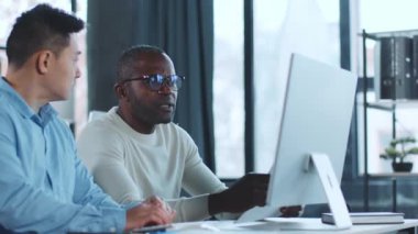 İki adam bir masada oturuyor, önlerindeki bilgisayar ekranına odaklanıyor..
