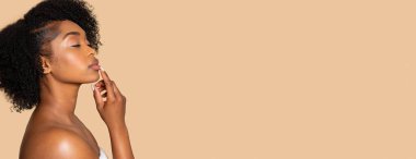 Dalgın, kıvırcık saçlı genç bir kadın, parmakları dudaklarında, geniş bej arka plan, panorama, pankart karşısında boş alan gösteriyor.