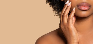 Siyah kadın dudaklarının yakın çekimi ve narin el hareketi, kıvırcık saçları ve bej arka planda kusursuz cildiyle vurgulanmış.