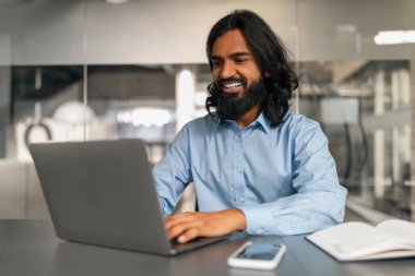 Rahat, profesyonel bir adam, rahat bir ofis ortamında dizüstü bilgisayarıyla çalışıyor.