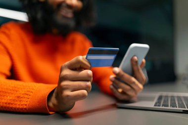 Neşeli bir adamın cep telefonu ve kredi kartı kullanması, muhtemelen online alışveriş yapması ya da finansmanı yönetmesi.
