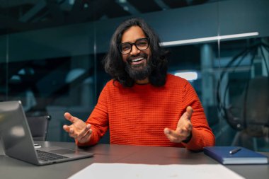 Hareketli bir süveter giyen biri çalışma masasında bir şeyler anlatıyor ya da öğretiyor gibi görünüyor.