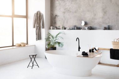 Geniş, güneşli banyo, gösterişli serbest banyo küveti, minimalist modern dekorlu hafif stil oda ve şehir manzaralı geniş pencere, kopyalama alanı.
