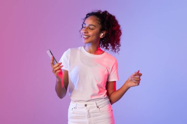 Canlı bir neon arka planda, kıvırcık saçlı bir kadın el hareketi yaparken akıllı bir telefon tutar.