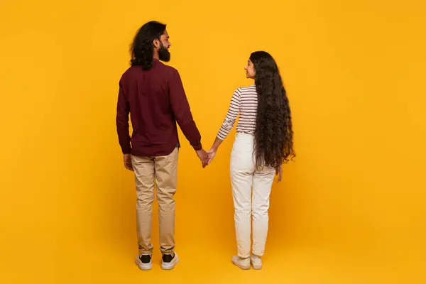 A rear view of a man and woman walking away hand in hand, the yellow backdrop evokes warmth and optimism in future paths