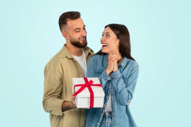 Neşeli beyaz adam mavi stüdyo geçmişinden dolayı karısını tebrik etmek için hediye paketi veriyor. Romantik tatili kutlayan genç bir çift. Yıldönümü konsepti, doğum günü sürprizi