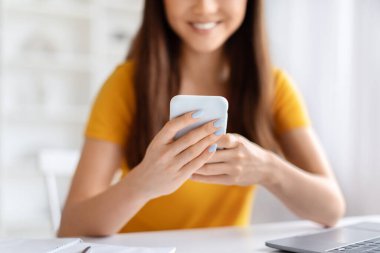 Gülümseyen Asyalı kadın akıllı telefonunu kullanıyor, mesajlaşıyor ya da internette geziniyor, modern ofis ortamında dizüstü bilgisayarla otururken Koreli genç bir kadının cep telefonuyla mesajlaşması tanınmaz hale geliyor.