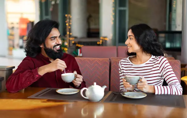 Happy young indian couple have romantic date at cafe. Cheerful eastern man and woman sitting at coffee shop, drinking tea, have conversation, enjoying time together. Love, relationships