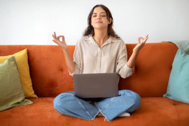 Zen kavramı. Genç bir kadın dizüstü bilgisayarla koltukta oturuyor ve gözleri kapalı meditasyon yapıyor, stresle ve endişelerle baş eden sakin bir kadın serbest çalışıyor, İç İşleri Bakanlığı 'nda bilgisayarla uğraşırken yoga yapıyor.