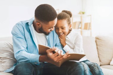 Cute afro girl and loving father enjoying time together, reading book, free space