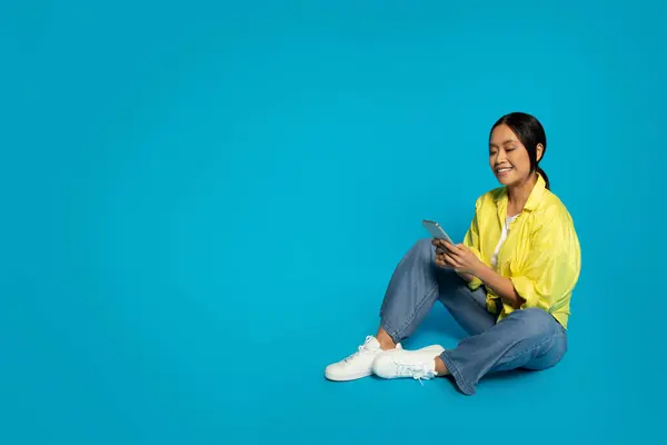 Sarı Ceketli Kot Pantolonlu Mutlu Bir Asyalı Kadın Telefonuyla Çarpıcı — Stok fotoğraf