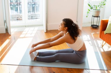 Genç bayanın ayak parmaklarını mindere değdirmesi, oturma pozisyonunda egzersiz yapması, evde fiziksel ve zihinsel sağlık için sağlık ve aktif egzersiz yapması. Yan görünüm
