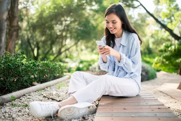 Smiling European Young Woman Casual Attire Absorbed Her Smartphone While — Stock Photo, Image