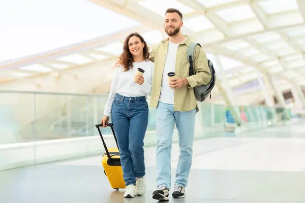 明るい黄色のスーツケースでコンテンポラリーな空港を気軽に歩くリラックスした若いカップル — ストック写真