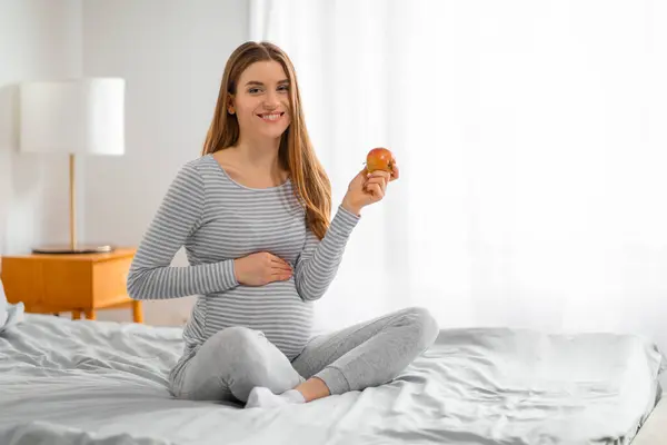 Cheerful Pregnant Woman Sits Cross Legged Bed Holding Apple Promoting — Stock Photo, Image
