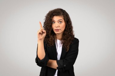 Parmağını kaldırmış takım elbiseli bir kadın. Uyarıyı veya önemli bir noktayı işaret ediyor.