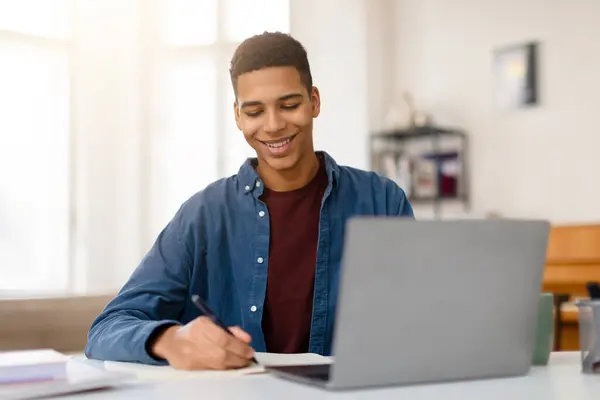 Joven Hombre Contento Sonriendo Mientras Escribe Notas Con Bolígrafo Portátil —  Fotos de Stock
