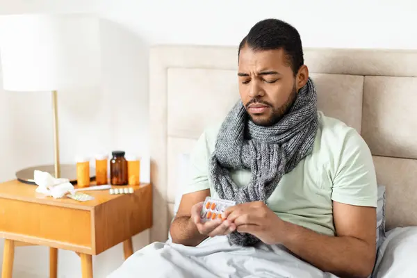 一位身体不舒服的非洲裔美国人坐在床上 四周都是药瓶 他在想该吃什么药 — 图库照片