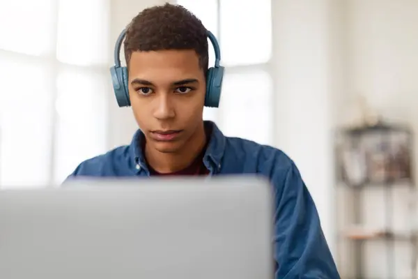青いヘッドフォンを持つ焦点を当てた若い男性は 意図的に画面を見ているラップトップ上で動作します — ストック写真