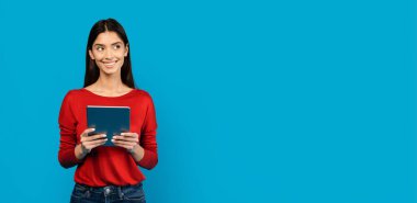 Kırmızı gömlekli kadın elinde dijital tabletle fotokopi odasına bakıyor. Mavi Stüdyo 'nun arka planına karşı duran mutlu kadın.