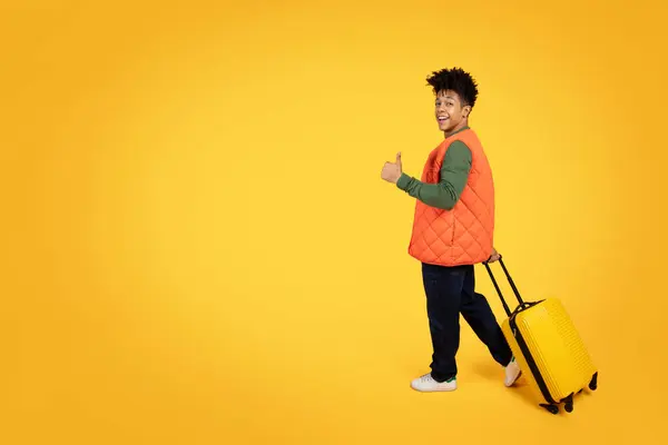 一个快乐的年轻的非洲裔美国人一边提着一个黄色的手提箱 一边提着一个生机勃勃的黄色背景 一边竖起大拇指 — 图库照片