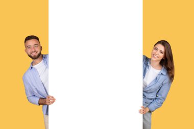 Kadın ve erkek gülümsüyor ve sarı arka planda beyaz boş bir pankart gösteriyor.