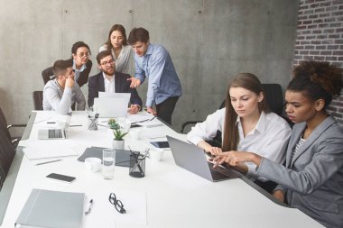 Çeşitli profesyonellerden oluşan bir grup, modern ekipmanlarla iyi ışıklandırılmış, çağdaş bir ofis alanında bir proje üzerinde çalışıyor.
