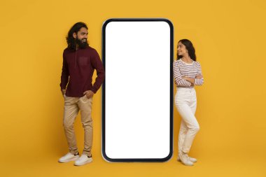 Erkek ve kadın büyük boş bir akıllı telefon ekranının her iki tarafında, sarı arka plandaki etkileşimi taklit ediyorlar.