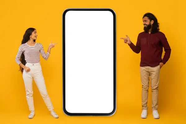 男性と女性は明るい黄色の背景に大きな空白のスマートフォン画面と相互作用する — ストック写真