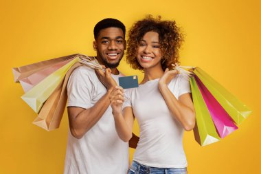 Mutlu müşteriler. Neşeli siyah adam ve kadın turuncu arka planda alışveriş torbaları ile gülümseyen, kredi kartı tavsiye, Panorama