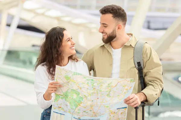 Loving couple share a cheerful moment as they look at each other over a map, suggesting shared travel plans in airport surroundings