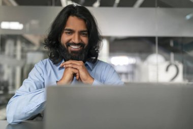 Mavi gömlekli neşeli bir adam hoş bir video görüşmesi yapıyor ya da bilgisayarla sanal bir toplantı yapıyor.