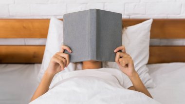 Sabahleyin yatakta yatan kadın kapsayan yüz ve kitap okuma
