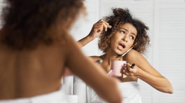 Afro-Amerikalı kız acele makyajını yaptı, kahve içti ve aynı anda banyoda aynanın önünde telefonla konuştu. Modern kadın konseptinin sabahı