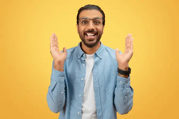 一个热情洋溢的印度男人 戴着眼镜 在一个充满活力的黄色背景下做着巨大的手势 — 图库照片