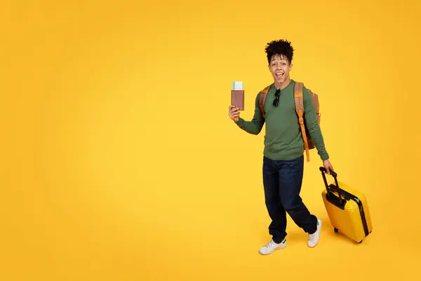 一个快乐的年轻的非洲裔美国人 拿着护照 拿着一个黄色的手提箱 准备旅行 背景是黄色的 — 图库照片