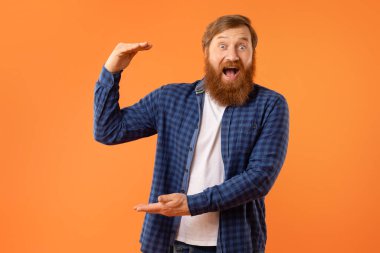Mutlu kızıl sakallı adam elinde görünmez bir ürün tutuyor, turuncu stüdyo arka planında boş bir yer gösteriyor, iyi bir servis öneriyor ya da öneriyor.