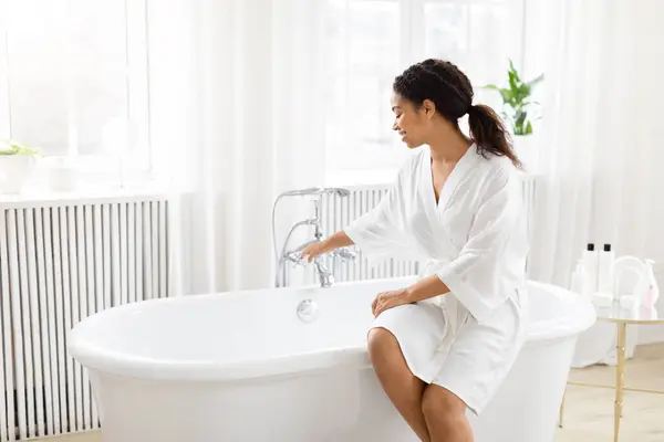 在现代化的浴室里 非洲裔美国女人正坐在一个时髦浴缸的边缘 — 图库照片