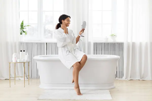 在灯火通明的浴室里 一个非洲裔美国女人对着一面手持的镜子唱歌很开心 很开心 — 图库照片