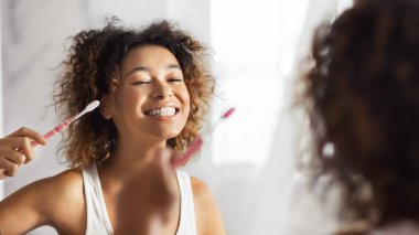 Gülümseyen genç afro kadın banyo, diş fırçası temizlik dişleriyle. Sağlıklı dişler kavramı