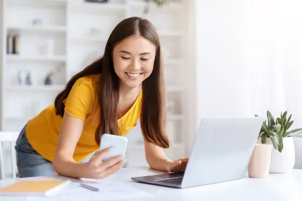 Smiling Asian Woman Yellow Top Using Cellphone Laptop Simultaneously Her — Stock Photo, Image