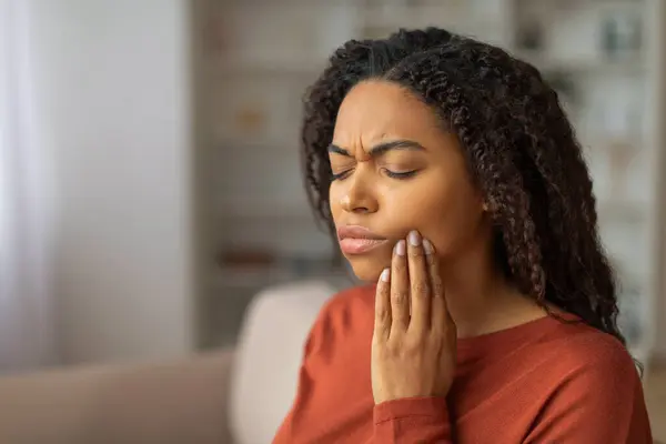 一位年轻的黑人妇女紧贴着她的脸颊 由于可能的牙痛表现出不适 非洲裔美国女性在家里感觉不适 复制空间 — 图库照片