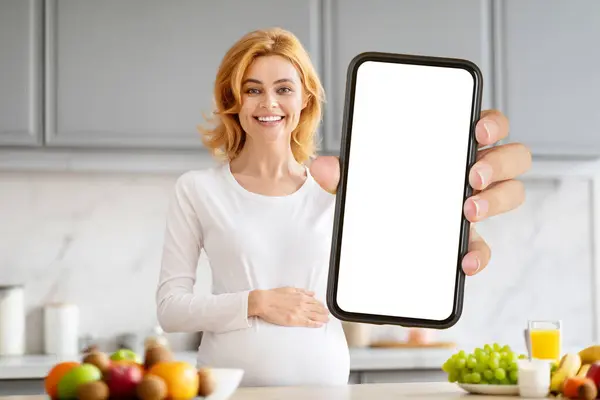 Očekávaná Dáma Představuje Prázdný Displej Smartphone Ovocem Naplněné Kuchyně Pozadí — Stock fotografie