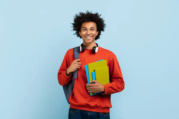 Uśmiechnięty Młody Afrykański Student Słuchawkami Szyi Niesie Książki Niebieskim Tle — Zdjęcie stockowe