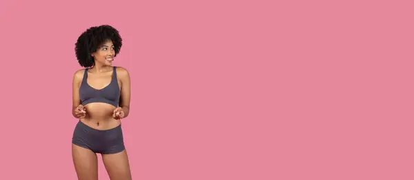 ピンクの背景で自分に向かってジェスチャーするスポーツ服で遊び心のある若い黒人女性 — ストック写真