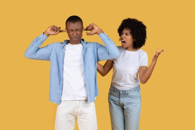 Afro-Amerikalı genç bir çift, bir örtülü kulaklarla ayakta duruyor ve diğeri de bağırıyor. Bu da sarı arka planda bir anlaşmazlık olduğunu gösteriyor.