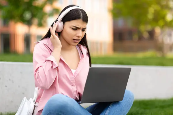 Zaniepokojona Młoda Dziewczyna Słuchawkami Patrzącymi Jej Ekran Laptopa Niespokojnym Wyrazem — Zdjęcie stockowe